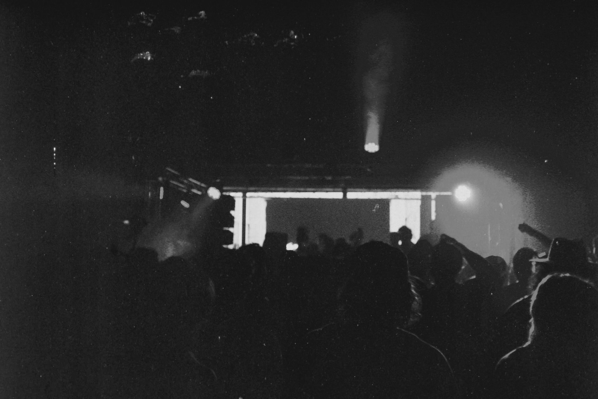 Crowd silhouettes and raised hands facing a stage in black and white.